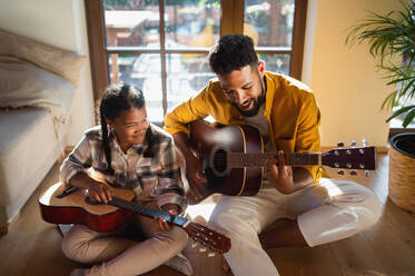 A high-angle view of happy father with small daughter indoors at home, playing guitar. - HPIF08655