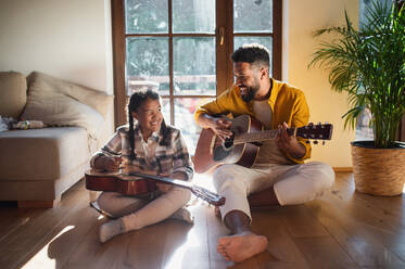 Frontansicht eines glücklichen Vaters mit seiner kleinen Tochter, die zu Hause Gitarre spielt. - HPIF08656