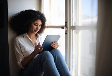 Porträt einer jungen Frau, die zu Hause auf der Fensterbank sitzt und ein Tablet benutzt. - HPIF08701