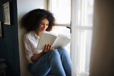 A portrait of young woman with book indoors at home, reading. - HPIF08702