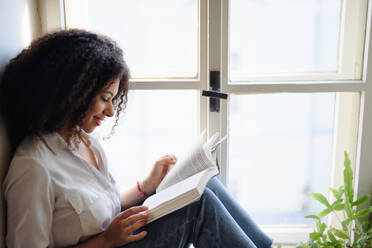Ein Porträt einer jungen Frau mit einem Buch, die zu Hause liest. - HPIF08704