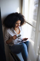 Porträt einer glücklichen jungen Frau mit Kaffee zu Hause, die ein Tablet benutzt. - HPIF08707