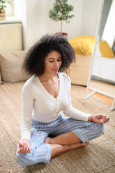 Ein Porträt einer jungen Frau, die zu Hause auf dem Boden Yogaübungen macht. - HPIF08715