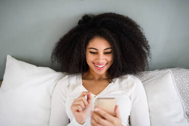Top view portrait of happy young woman indoors on bed, using smartphone. - HPIF08725