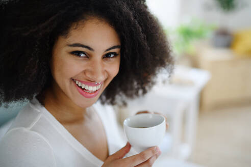 Nahaufnahme eines Porträts einer lachenden jungen Frau mit Kaffee in einem Raum, die in die Kamera schaut. - HPIF08729