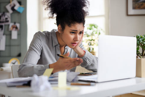 Frustrierte junge Frau mit Laptop arbeitet drinnen zu Hause, Home-Office-Konzept. - HPIF08750