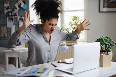 Frustrated young woman with laptop working indoors at home, home office concept. - HPIF08751