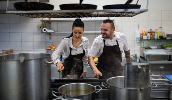 A chef and cook cooking together indoors in restaurant kitchen. - HPIF08766