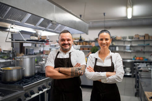 A confident chef and cook standing with arms crossed and looking at camera in commercial kitchen. - HPIF08773