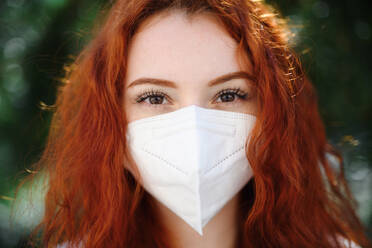 A close-up portrait of young woman with respirator looking at camera outdoors in city, coronavirus concept. - HPIF08789