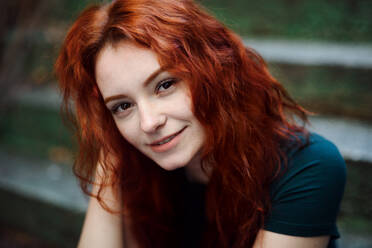 A portrait of young woman sitting outdoors on staircase in city, looking at camera. - HPIF08791