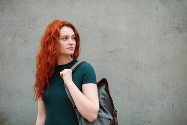 Porträt einer jungen Frau mit Rucksack, die im Freien vor einem grauen Hintergrund steht, Kopierraum. - HPIF08795