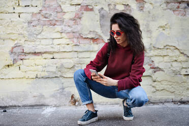 Ein Porträt einer jungen Frau, die im Freien auf einer Straße in der Stadt steht und ein Smartphone benutzt. - HPIF08807