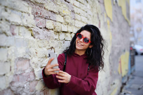 Eine junge Frau hält einen Moment in der Stadt mit ihrem Smartphone fest und macht ein Selfie vor dem Hintergrund der Straße - HPIF08809