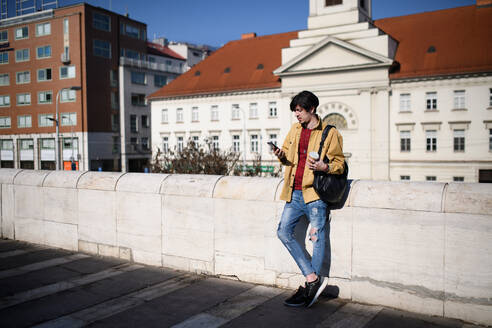 Ein Porträt eines jungen Mannes, der in der Stadt im Freien steht und sein Smartphone benutzt. - HPIF08815