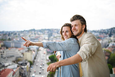 Ein glückliches, verliebtes junges Paar, das auf dem Balkon seines Hauses steht, sich umarmt und unterhält. - HPIF08835