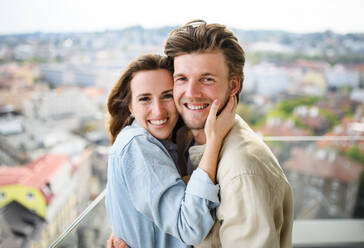 Ein glückliches, verliebtes junges Paar, das auf dem heimischen Balkon in die Kamera schaut und sich umarmt. - HPIF08838