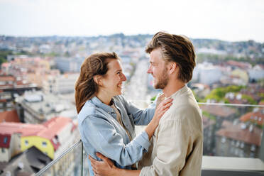 A happy young couple in love standing outdoors on balcony at home, looking at each other. - HPIF08839