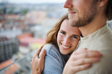 Ein glückliches, verliebtes junges Paar steht im Freien auf dem Balkon seines Hauses und umarmt sich. - HPIF08841
