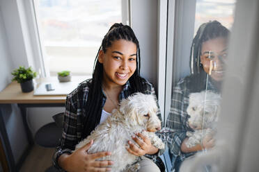 Ein Porträt eines glücklichen Teenagers mit Hund, der zu Hause sitzt und in die Kamera schaut. - HPIF08844