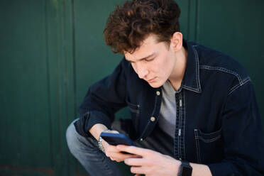 Ein Porträt eines jungen Mannes vor grünem Hintergrund im Freien, der ein Smartphone benutzt. - HPIF08853