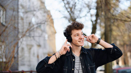 Ein Porträt eines jungen Mannes, der mit Kopfhörern in der Stadt spazieren geht und Musik hört. - HPIF08856