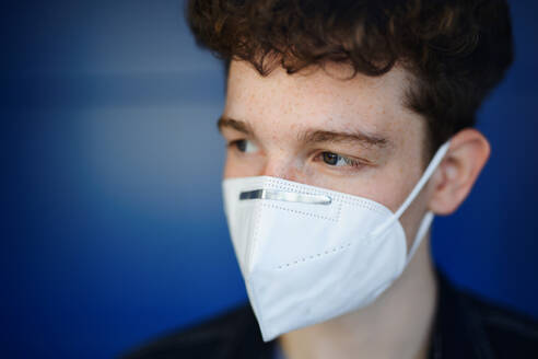 Ein Kopfporträt eines jungen Mannes mit Atemschutzmaske vor grünem Hintergrund im Freien, Coronavirus-Konzept. - HPIF08858