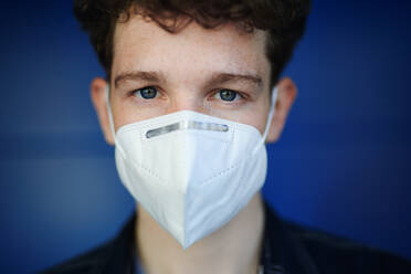 A headshot portrait of young man with respirator against green background outdoors, coronavirus concept. - HPIF08869