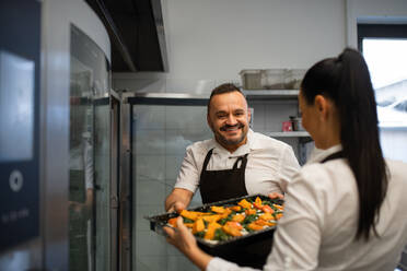 A chef and cook working on their dishes indoors in restaurant kitchen. - HPIF08876