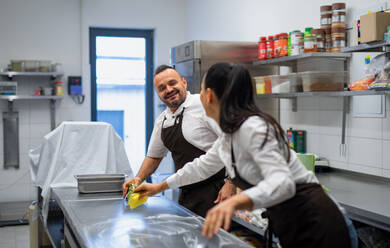 Ein Koch und eine Köchin säubern den Arbeitsbereich nach dem Abwasch in einer Restaurantküche. - HPIF08878