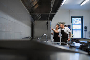 Ein Chefkoch unterrichtet einen Koch in der Verwendung eines Combi-Ofens in einer Restaurantküche. - HPIF08894