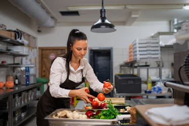 Eine professionelle weibliche Köchin, die drinnen in einer Restaurantküche Gemüse schneidet. - HPIF08895