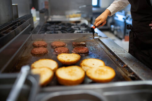 Eine Nahaufnahme einer professionellen Köchin, die in einer Restaurantküche Burger zubereitet. - HPIF08908