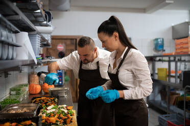 Ein Koch und eine Köchin arbeiten in der Küche eines Restaurants an ihren Gerichten. - HPIF08909