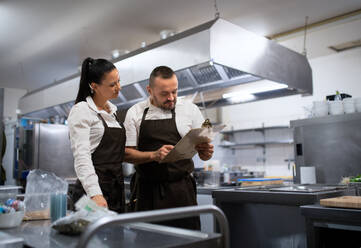 A chef and cook discussing menu indoors in restaurant kitchen. - HPIF08918