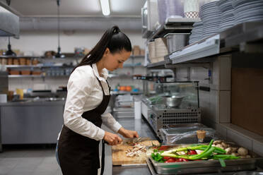 Eine professionelle weibliche Köchin, die drinnen in einer Restaurantküche Gemüse schneidet. - HPIF08920