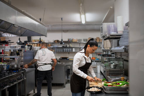 Eine professionelle weibliche Köchin, die drinnen in einer Restaurantküche Gemüse schneidet. - HPIF08923