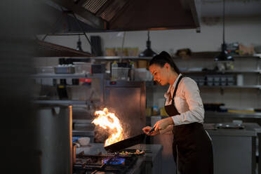 Ein professioneller Koch bereitet eine Mahlzeit zu, flambiert drinnen in einer Restaurantküche. - HPIF08929