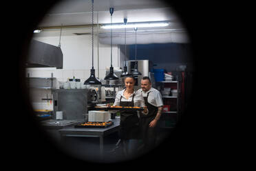 A happy chef and cook working on their dishes in restaurant kitchen, shot through circle door window. - HPIF08940