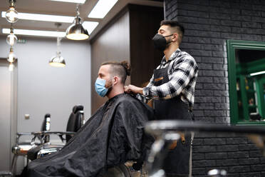 Man client visiting haidresser and hairstylist in barber shop, coronavirus and new normal concept. - HPIF08943