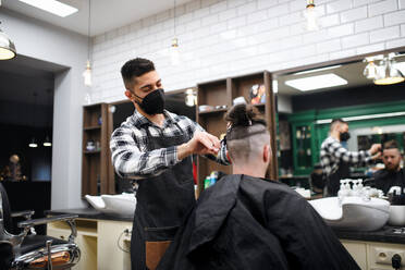 Ein männlicher Kunde besucht einen Friseur und eine Friseurin in einem Friseursalon, Coronavirus und das Konzept der neuen Normalität. - HPIF08944