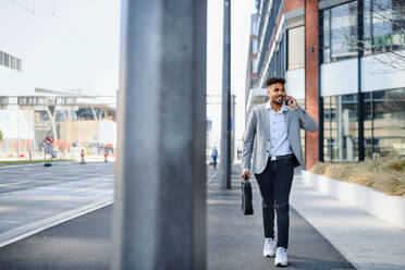 Ein Porträt eines jungen Mannes, der auf einer Straße in der Stadt spazieren geht und ein Smartphone benutzt. - HPIF08956