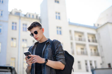 Ein Porträt eines jungen Mannes, der in der Stadt im Freien steht und sein Smartphone benutzt. - HPIF08965