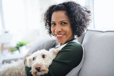 Ein Porträt einer glücklichen reifen Frau mit Hund, die zu Hause sitzt und in die Kamera schaut. - HPIF08977