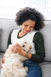 Ein Porträt einer glücklichen reifen Frau, die zu Hause sitzt und mit ihrem Hund spielt. - HPIF08979
