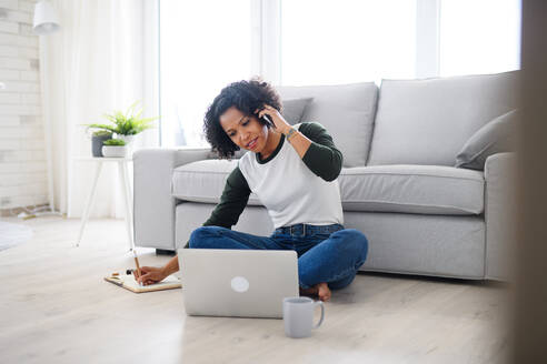 Ein Porträt der glücklichen reifen Frau arbeitet am Laptop und telefonieren drinnen, Home-Office-Konzept. - HPIF08980