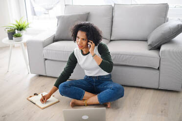 Ein Porträt der glücklichen reifen Frau arbeitet am Laptop und telefonieren drinnen, Home-Office-Konzept. - HPIF08981