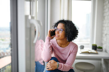 A portrait of happy mature woman making a phone call indoors, looking out of window. - HPIF08985