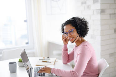 Ein Porträt der glücklichen reifen Frau mit Headset arbeiten am Laptop drinnen, Home-Office-Konzept. - HPIF08992