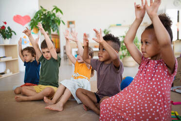 Eine Gruppe von kleinen Kindergartenkindern, die in einem Klassenzimmer auf dem Boden sitzen und spielen. - HPIF09008